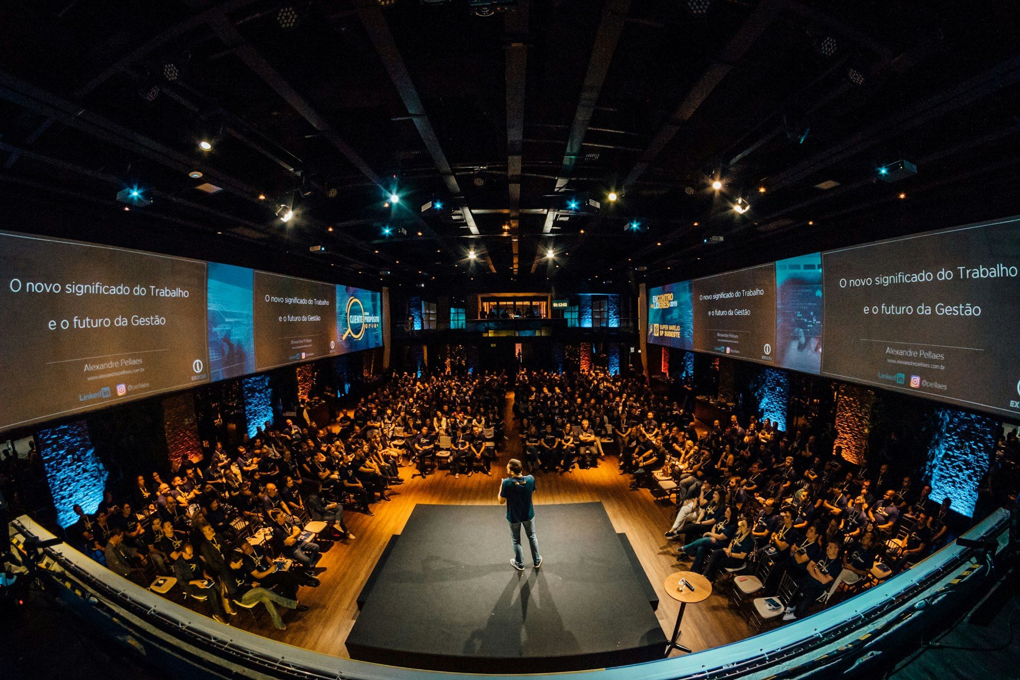 A speaker on stage in front of a large seated audience in a conference hall.