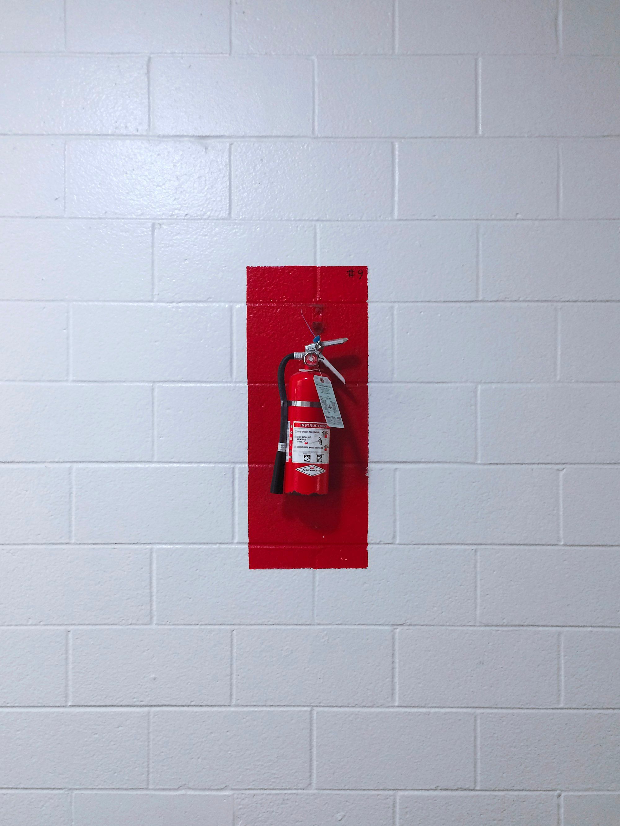 A red fire extinguisher mounted on a white brick wall.