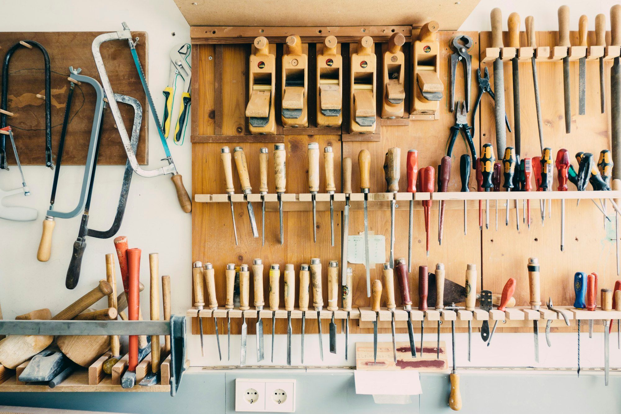 Hand tools hanging in rows on a workshop wall.