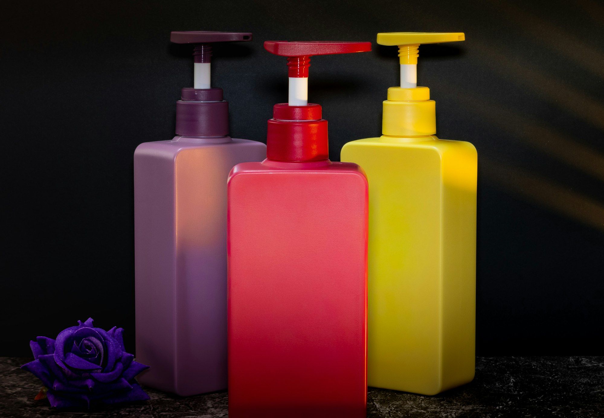 Three unlabelled pump bottles in purple, red and yellow.